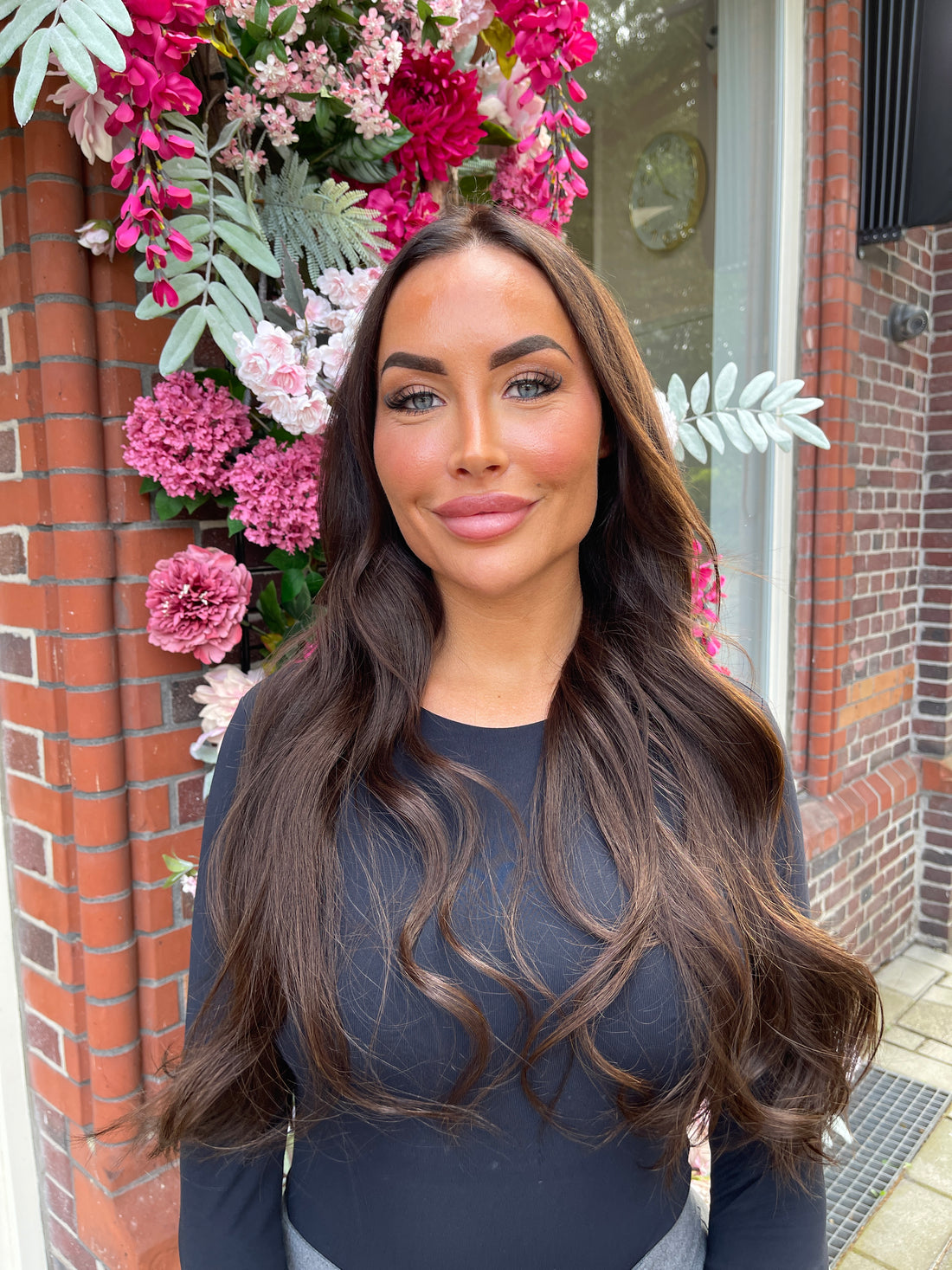 Lang donkerbruin golvend haar bij de bloemenwand van de salon